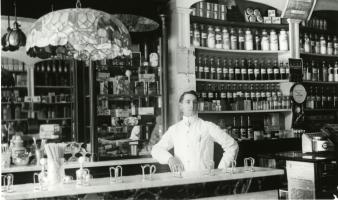Pharmacist in front of medicine shelves at Collette's drug store. Spencer Public Library.