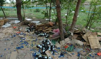 Bottles and trash cover the ground under some trees. 