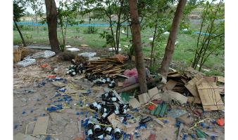 Plastic bottles and trash cover the ground under some trees.