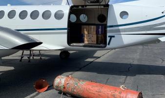 A large, orange metal tube in front of an airplane. 