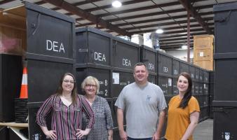 Four people pose for a picture in front of exhibit packing crates.