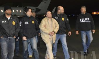 Four law enforcement officers transport a prisoner in handcuffs.