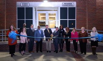 A group of people before a building cut a large blue ribbon.