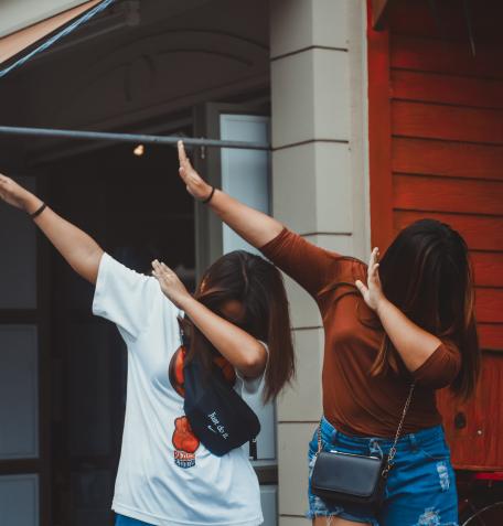 Two teenaged girls dabbing in front of a house