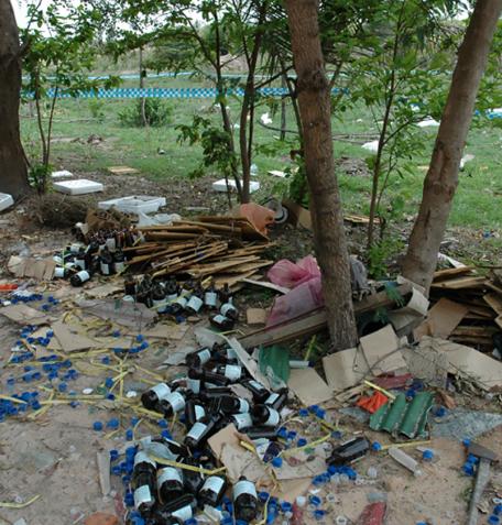 Bottles and trash cover the ground under some trees. 