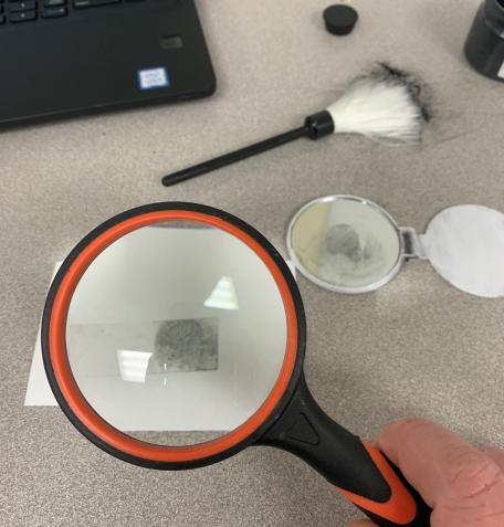 A hand holding a magnifying glass over a fingerprint. 