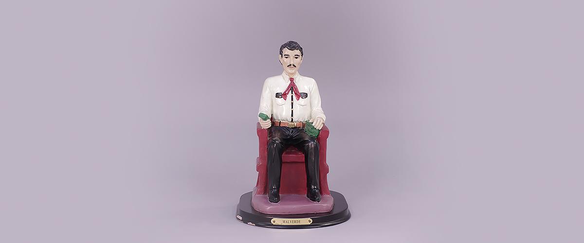   A painted statue of Jesús Malverde sitting in a chair.
