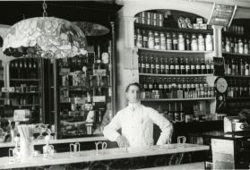 Pharmacist in front of medicine shelves at Collette's drug store. Spencer Public Library.
