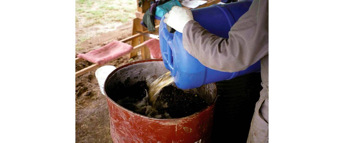 A person pouring gasoline inside a metal drum.