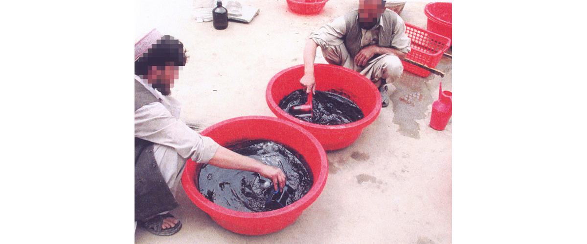 Two men stirring chemical solutions in red buckets 