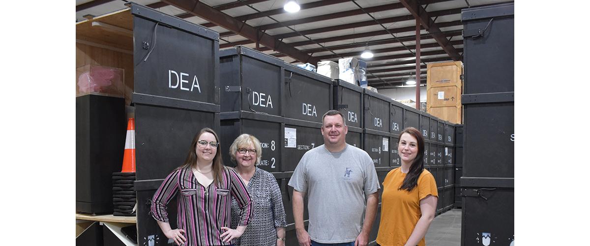 Four people pose for a picture in front of exhibit storage crates.