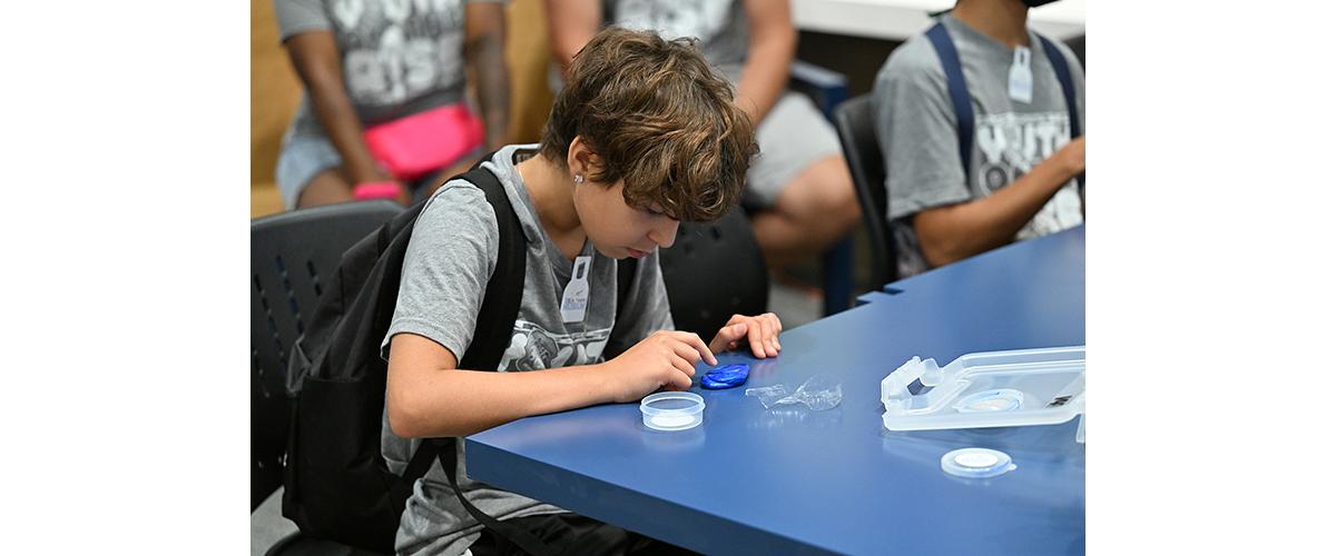 A young boy makes a fingerprint by pressing his finger into silly putty.