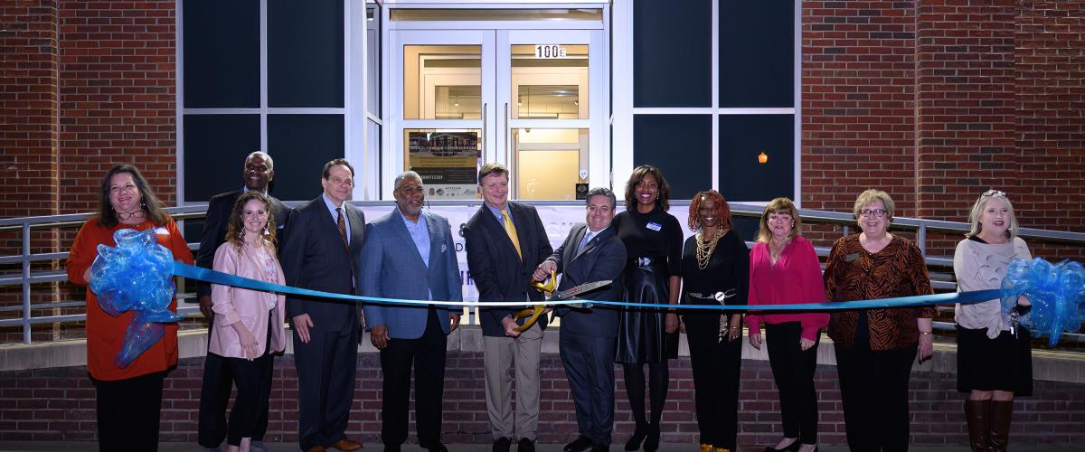 A group of people cut a large blue ribbon before a building.