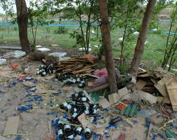 Bottles and trash cover the ground under some trees. 