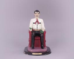 A painted statue of Jesús Malverde sitting in a chair.